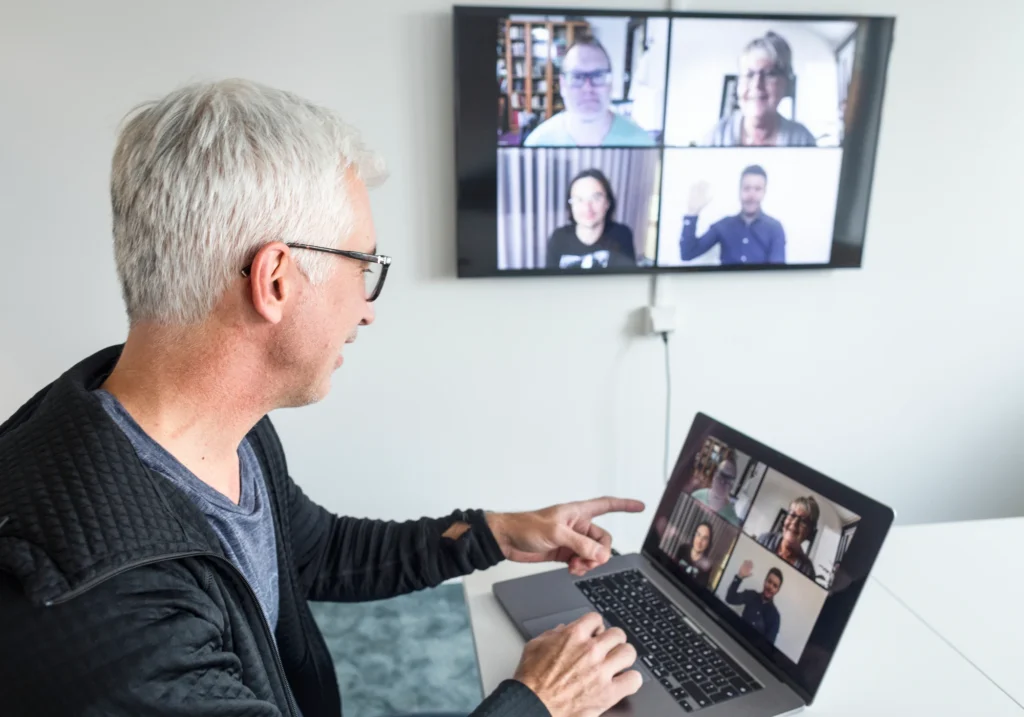 En man vid laptop har digitalt möte med flera.